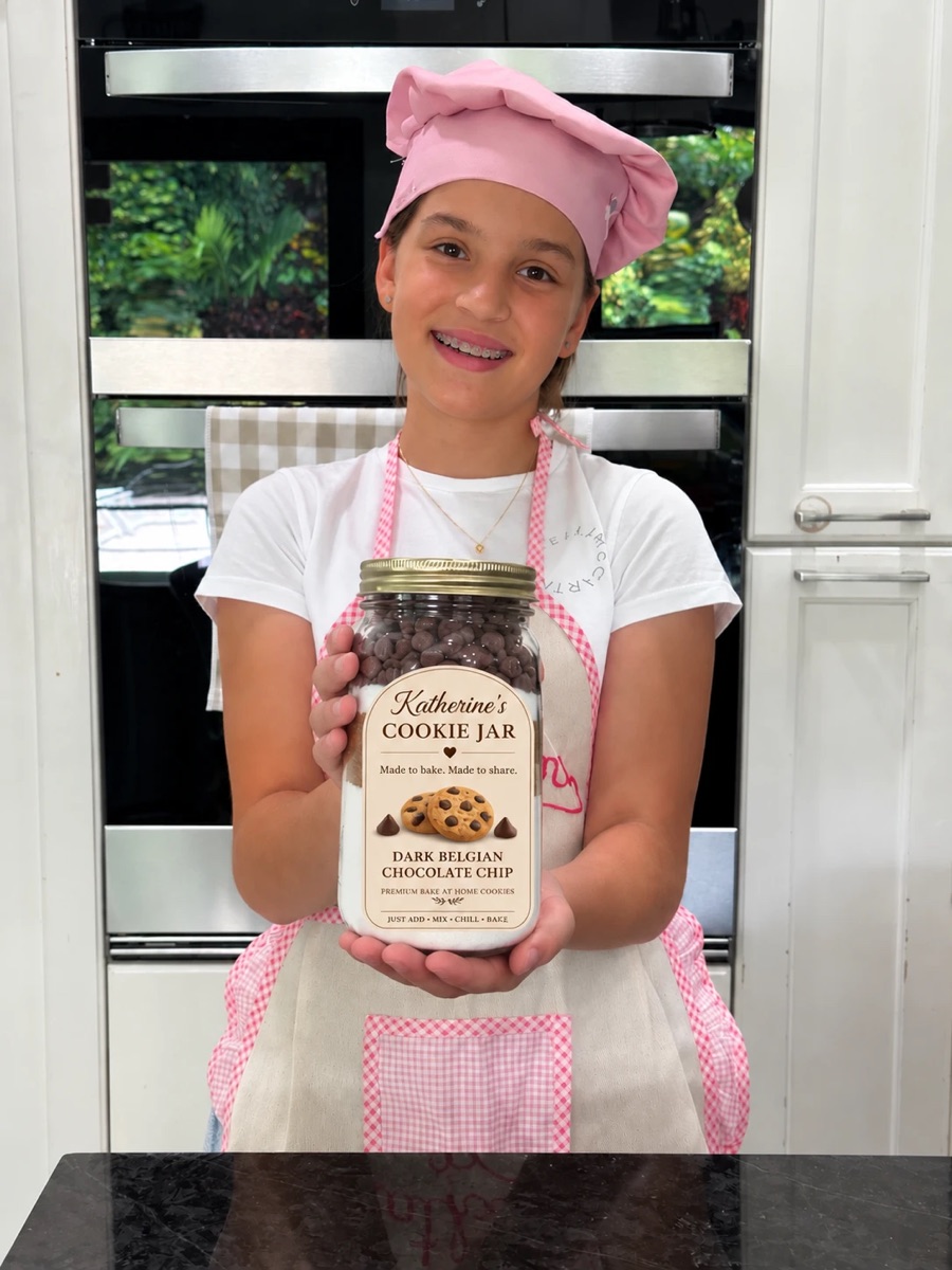 Katherine in a pink chef hat and apron, holding a Dark Belgian Chocolate Chip cookie jar in her kitchen